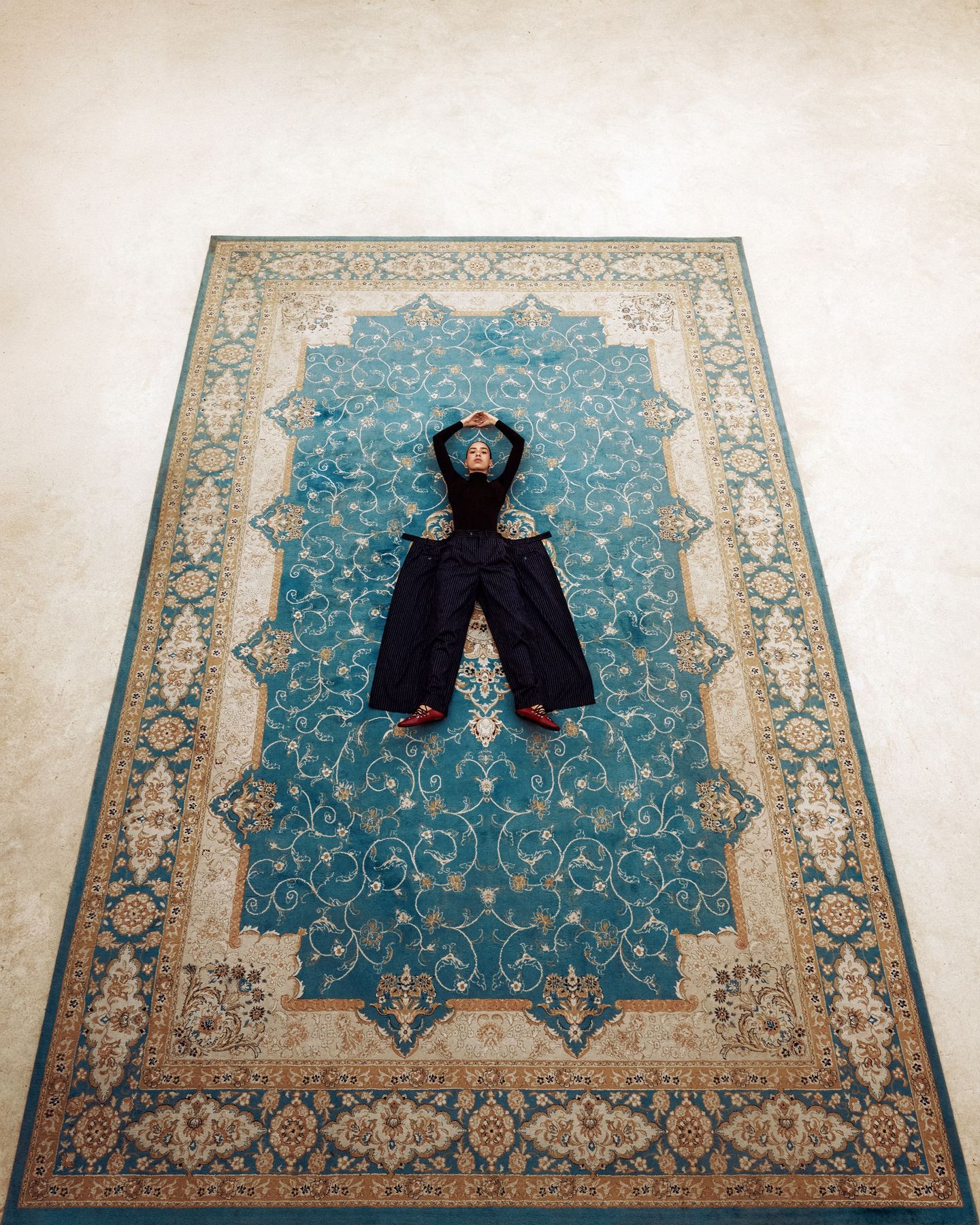 Model lying at the centre of a blue and gold Persian carpet, shot from above