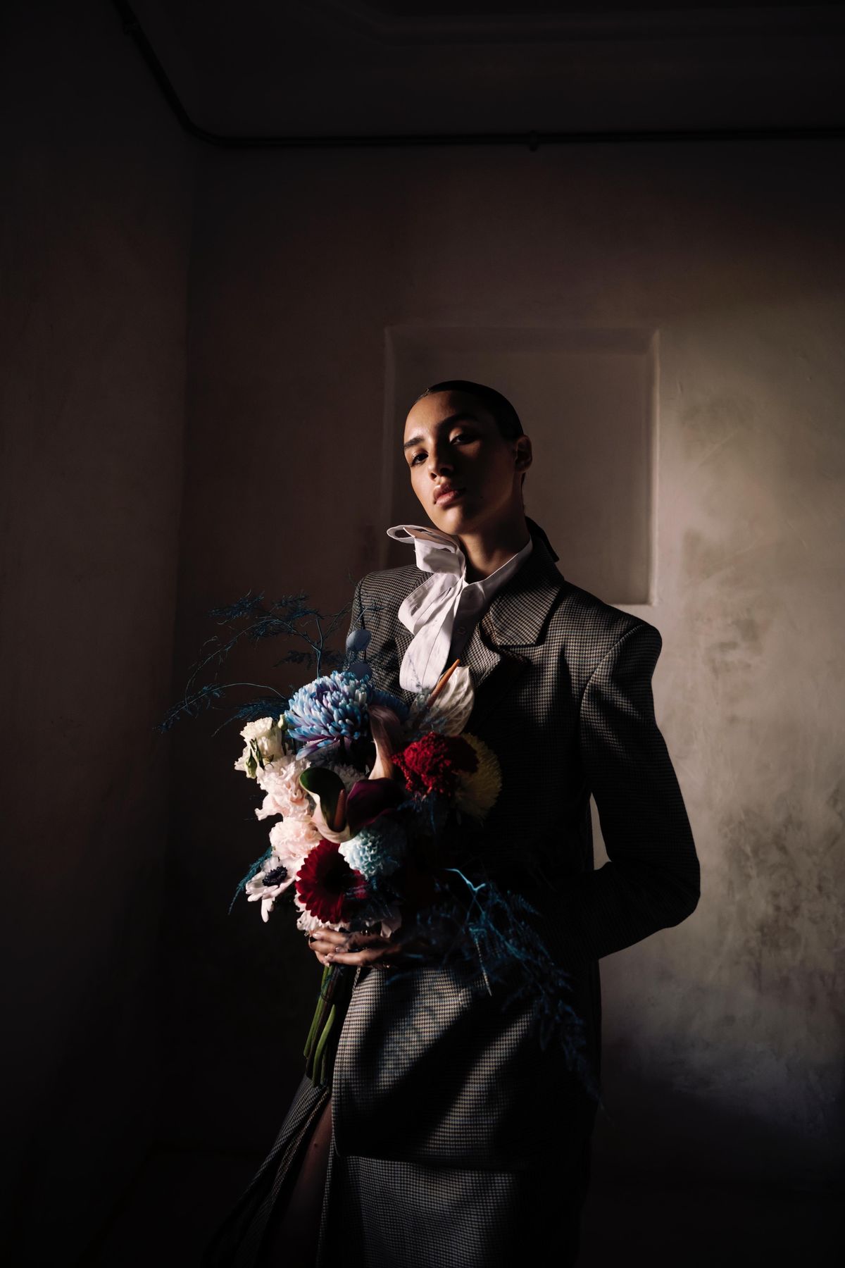 Model in a checked suit holding a bouquet in low, dramatic light