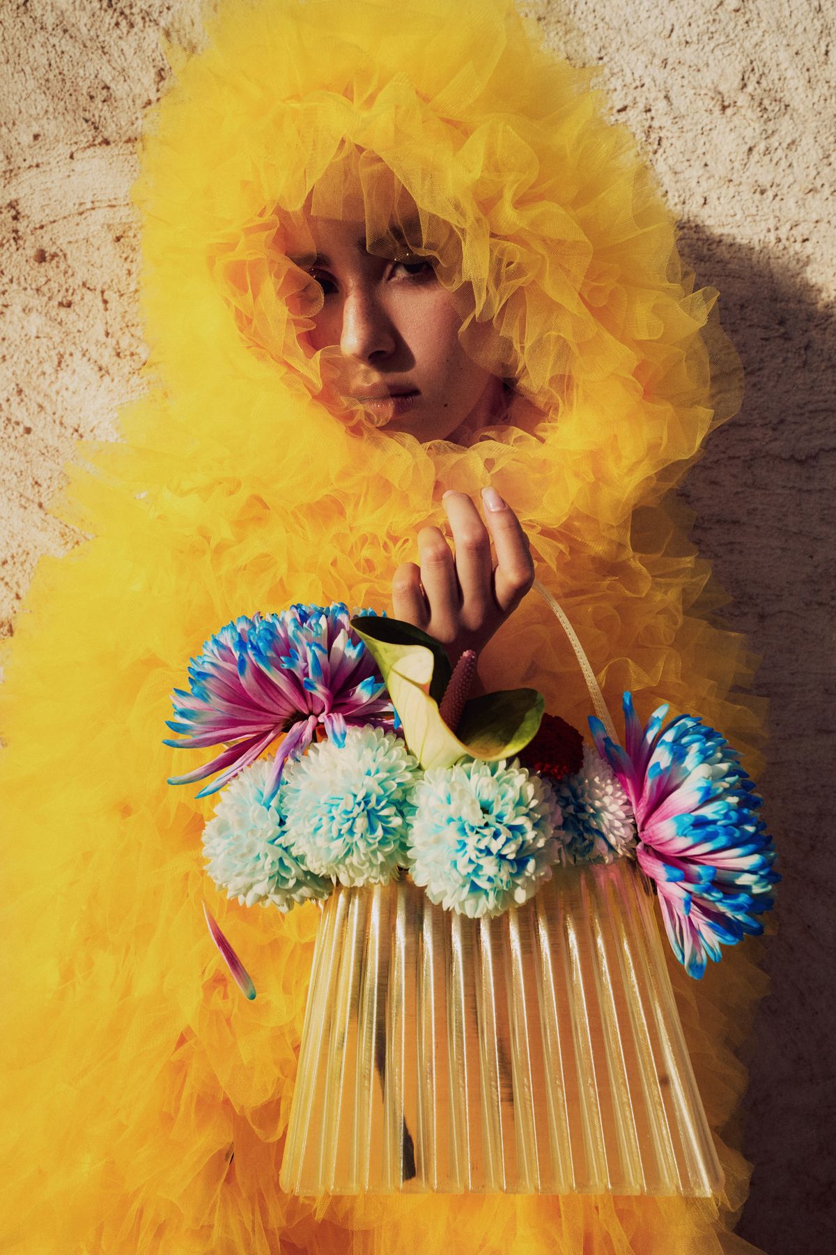 Model framed by yellow tulle holding a bag of bright flowers