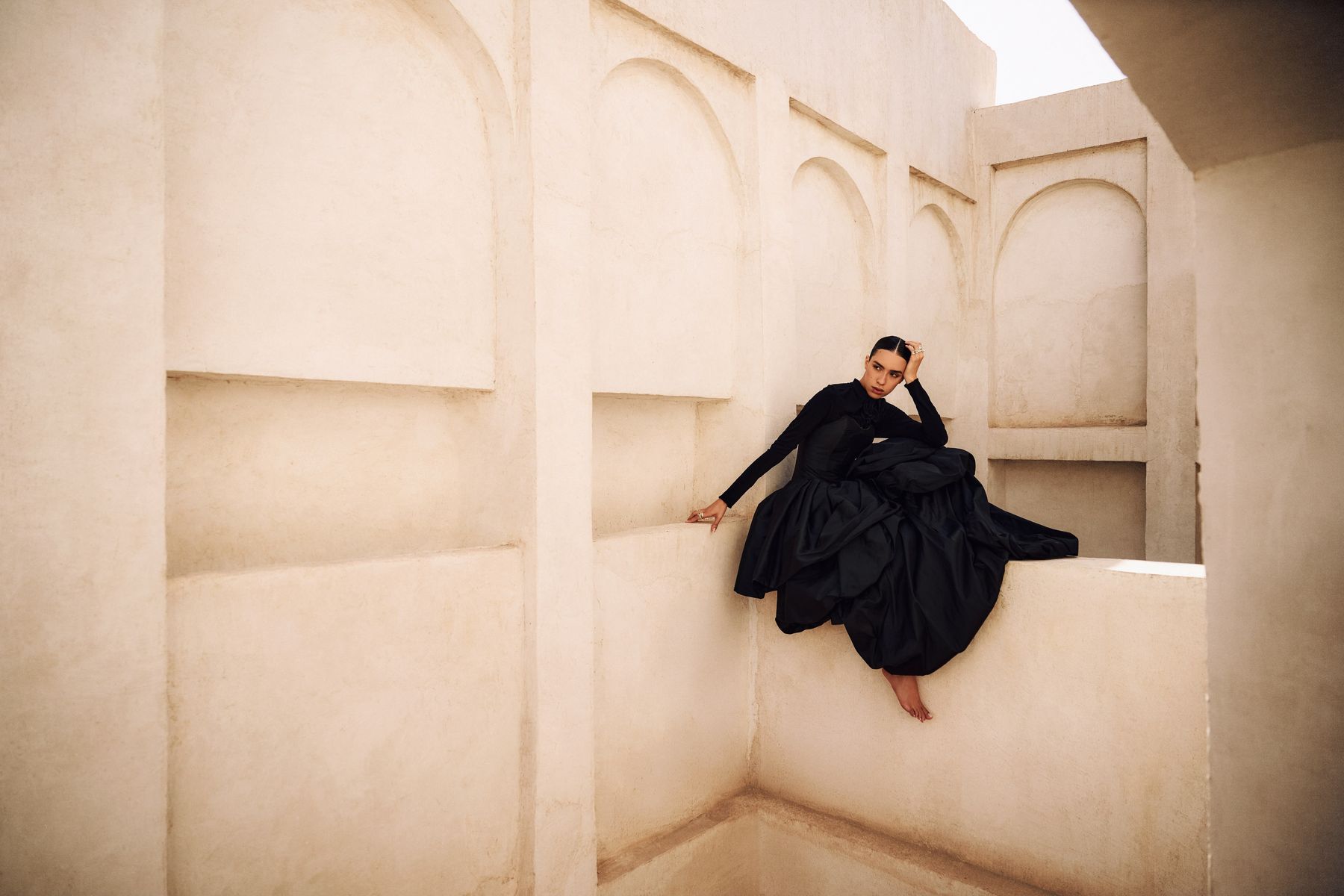 Model in a black gown seated within pale plaster alcoves