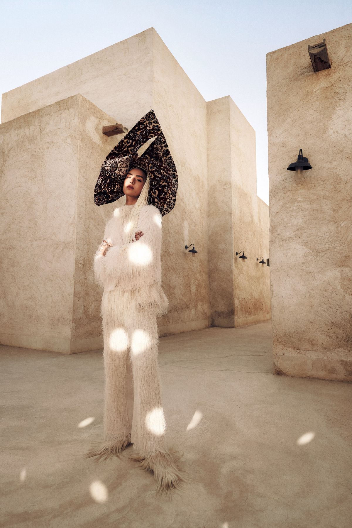 Model in cream fringing wearing a carpet headdress in a courtyard