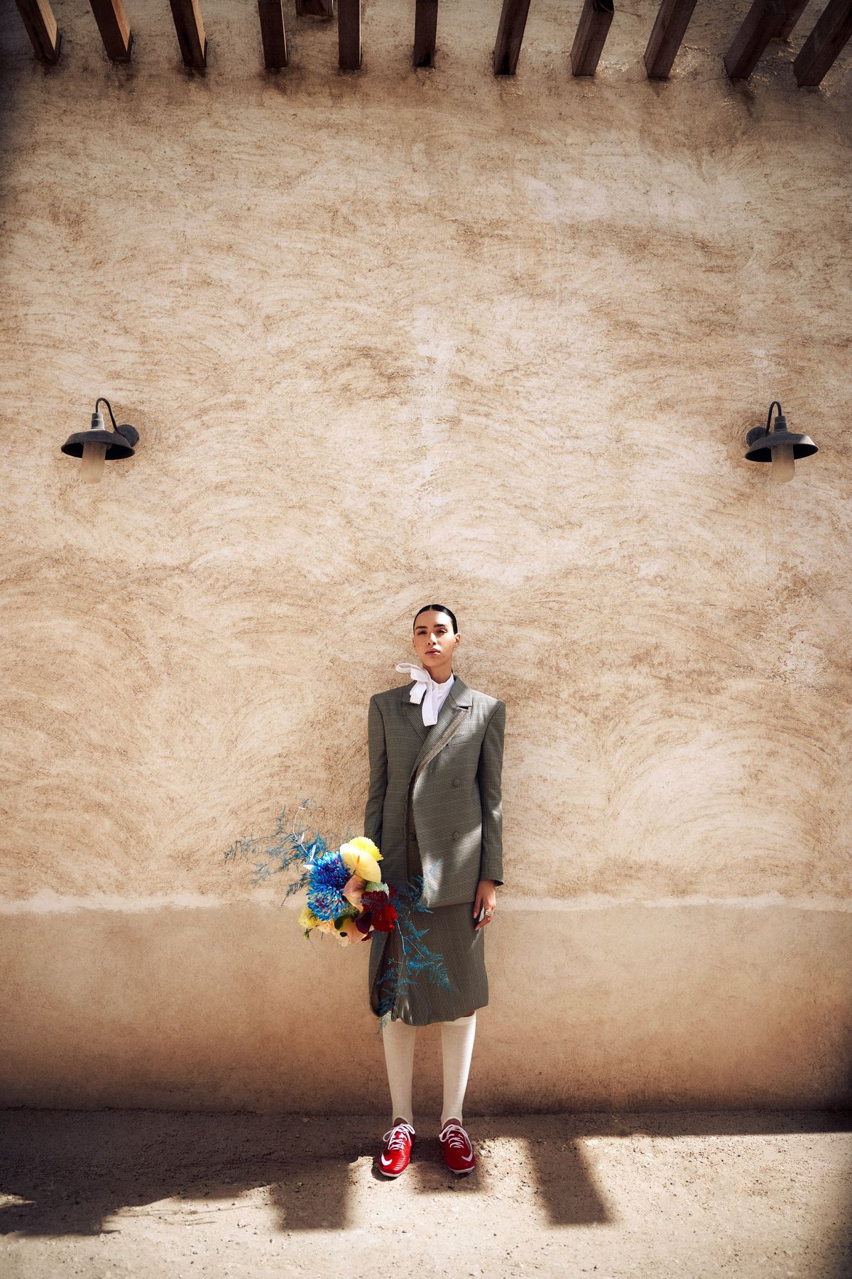 Model in a checked suit and red trainers against a textured wall