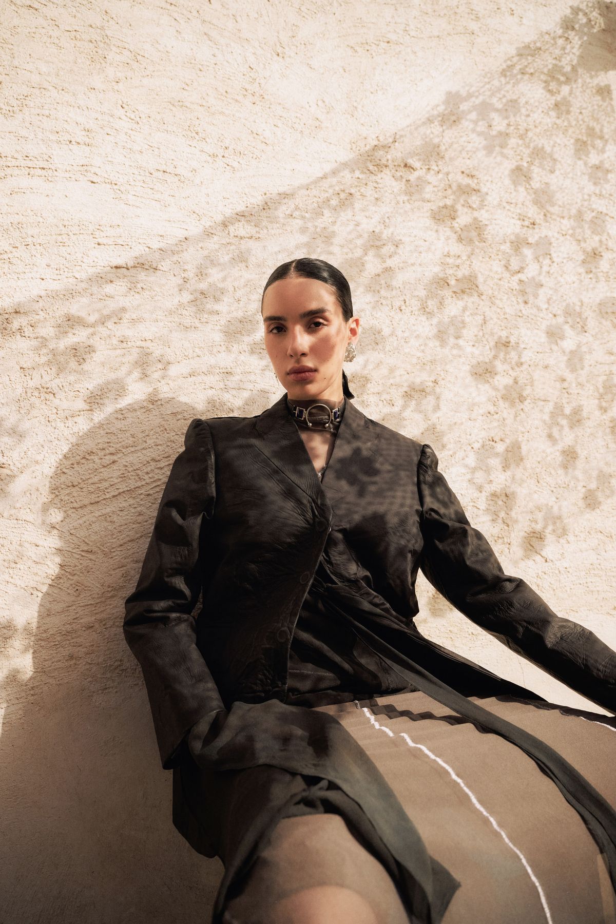 Model in dark leather reclining against a sunlit plaster wall