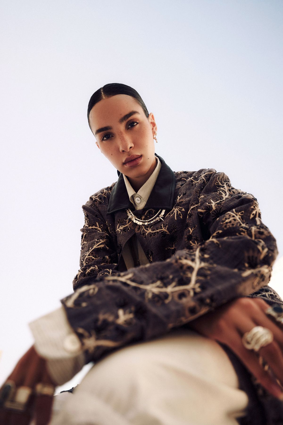 Model in an embroidered coat photographed from a low angle against the sky