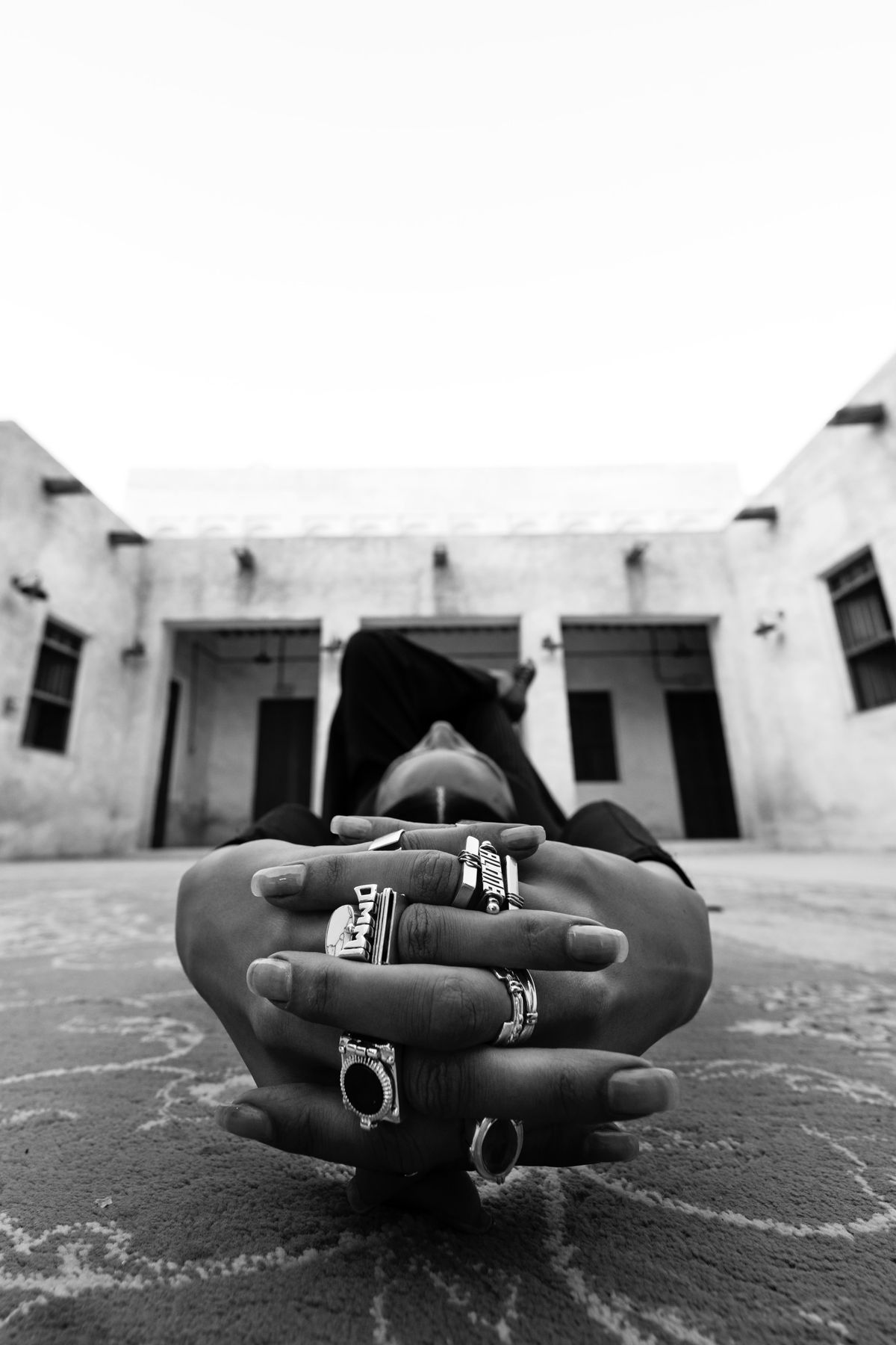 Black and white close-up of ringed hands with a courtyard beyond
